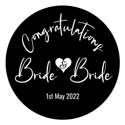 White curved "Congratulations" text. Below this is "Bride & Bride" text, the & is a black cutout in a white heart. With "1st May 2022" underneath. All white on a black circle.