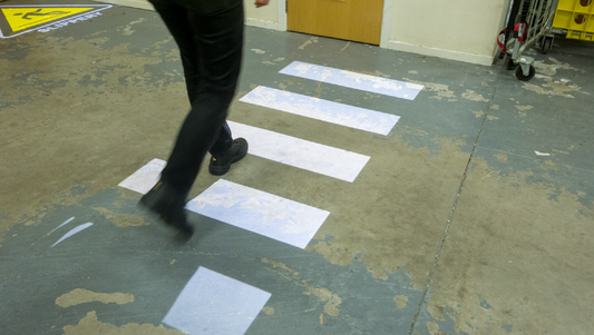 Projected safety signage of a zebra crossing on a warehouse floor.